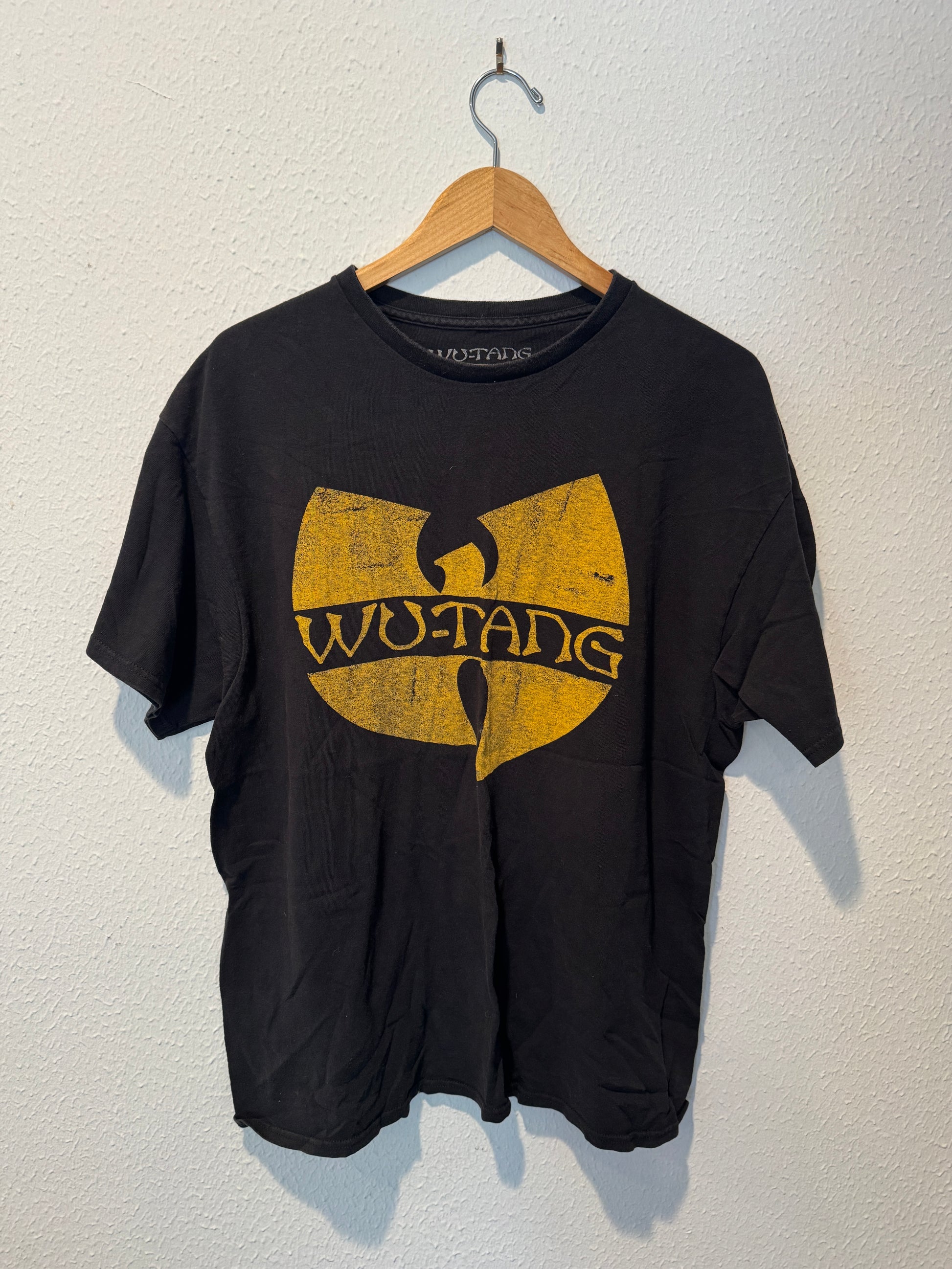 Black t-shirt with Wu-Tang Clan logo on a hanger against a white wall